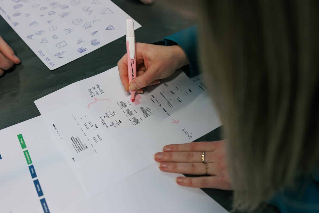 Een collega die een gepersonaliseerde proefdruk markeert met een markeerstift, een kleurenstrip en een vel pictogrammen op tafel