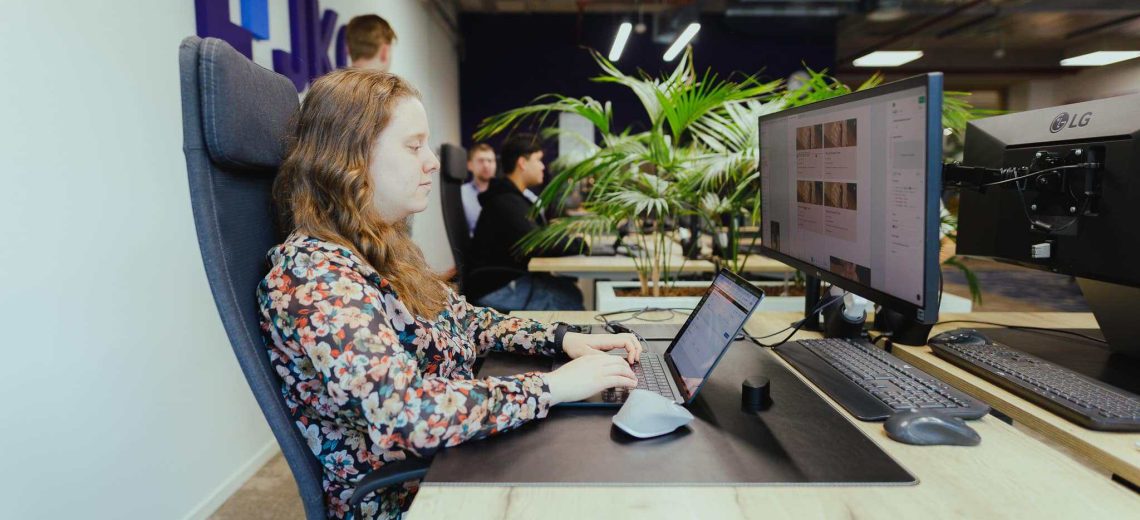 Een collega die aan een webapplicatie werkt achter twee beeldschermen