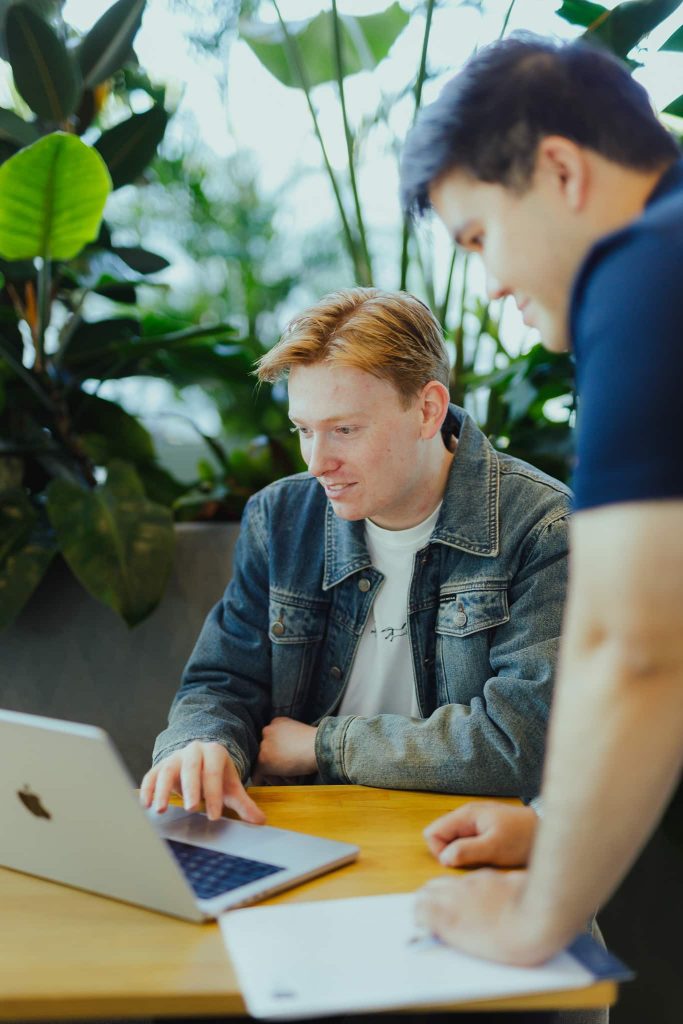 Two colleagues looking at a website together on a laptop, surrounded by plants