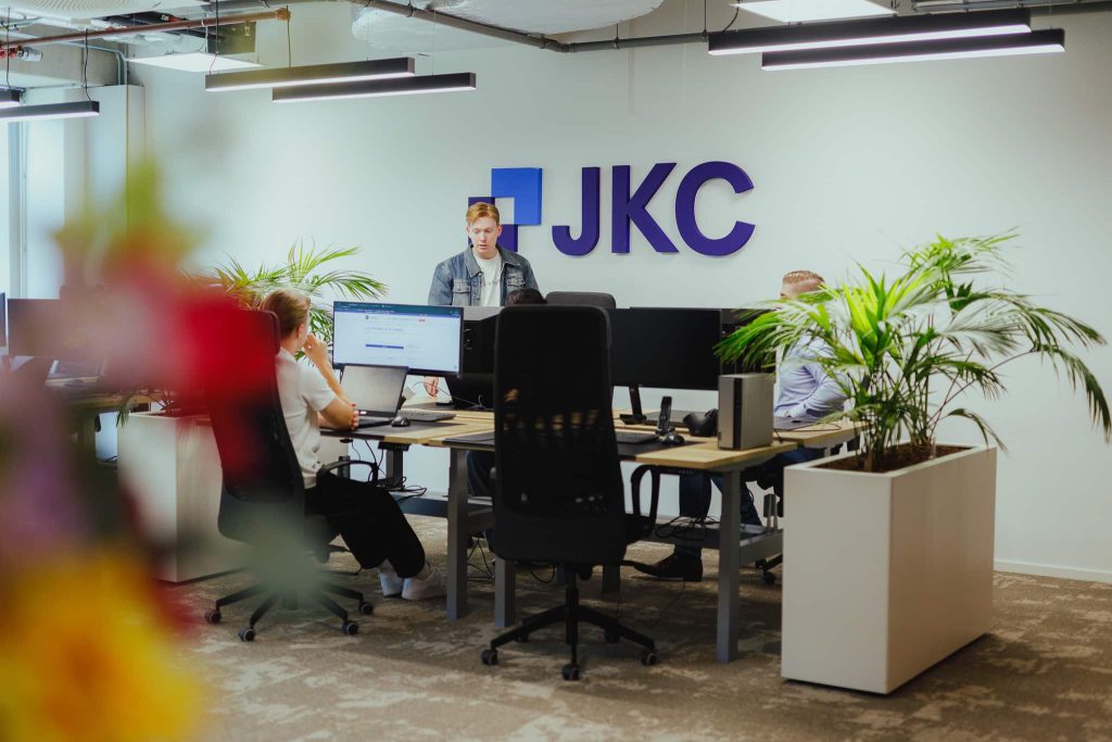 Het JKC-kantoor, met collega's aan het werk achter hun bureaus onder het JKC-logo