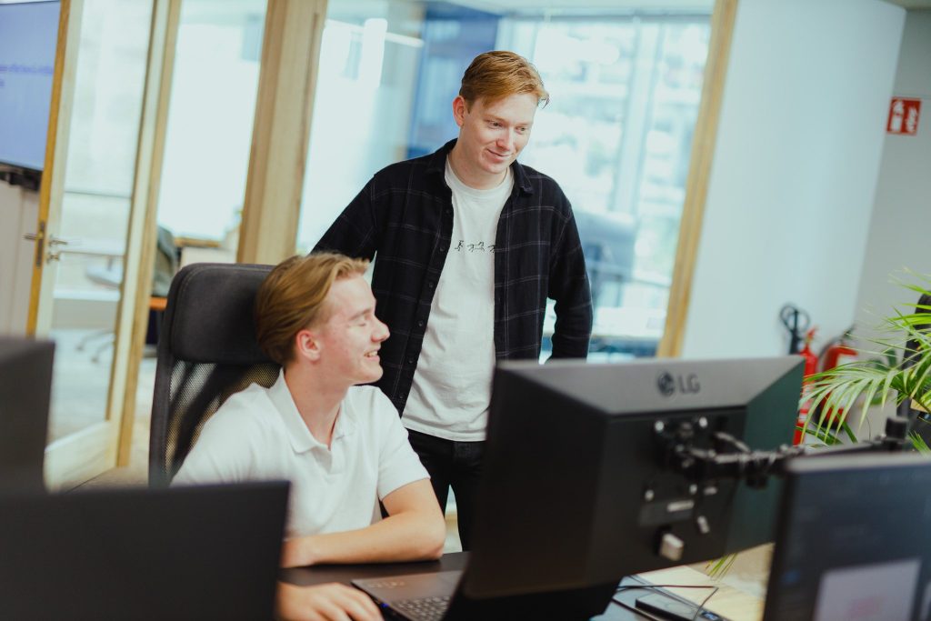 A colleague looking in on a workstation over a seated colleague’s shoulder