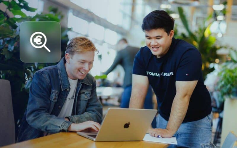 Google Ads cost: two colleagues looking at a laptop, with a magnifying glass and euro icon