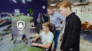 WordPress hacked: three JKC colleagues looking at a laptop next to a shield with a padlock