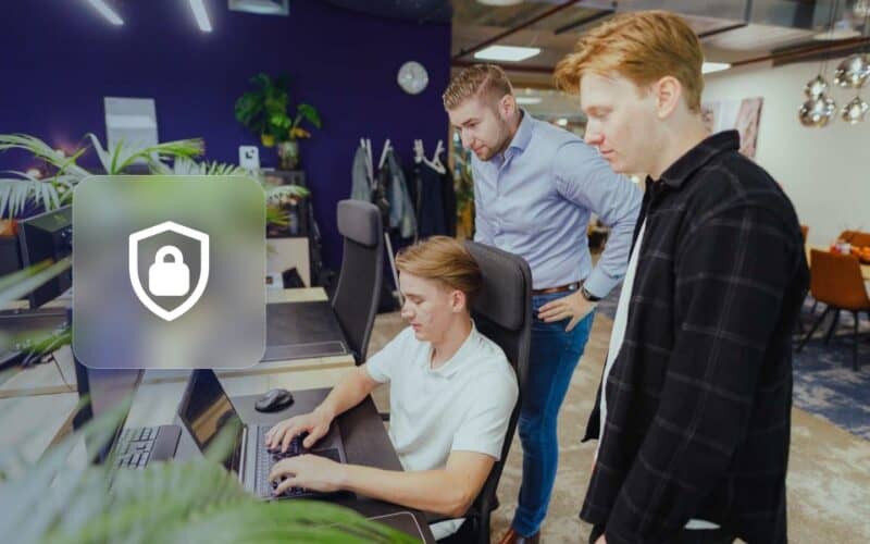 WordPress hacked: three JKC colleagues looking at a laptop next to a shield with a padlock